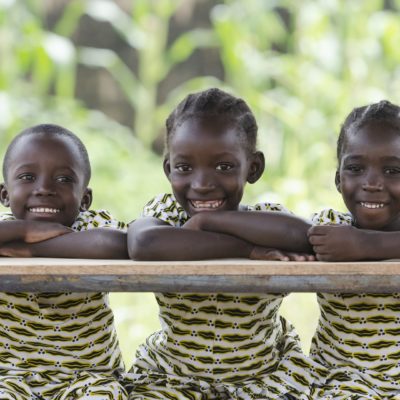 Three African children proudly sitting in their desk at school in Bamako, Mali. Candid outdoor shot of one boy and two girls learning their lessons at school.